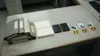 Ein grauer Bürotisch von schräg oben. Darauf liegen ordentlich aufgereiht ein Stapel grauer und beiger Aktenordner, zwei Stapel Papier, zwei schwarze externe Festplatten und drei USB-Sticks i