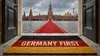 Blick durch eine geöffnete Flügeltür auf den Roten Platz in Moskau. Ein roter Teppich führt über das Kopfsteinpflaster zum Spasski-Turm des Kreml. Davor, auf der Türschwelle, liegt eine Fußma
