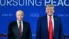 Donald Trump und Wladimir Putin stehen nebeneinander vor einer blauen Wand mit der Aufschrift „Pursuing Peace“. Trump lächelt, Putin blickt ernst in die Kamera.