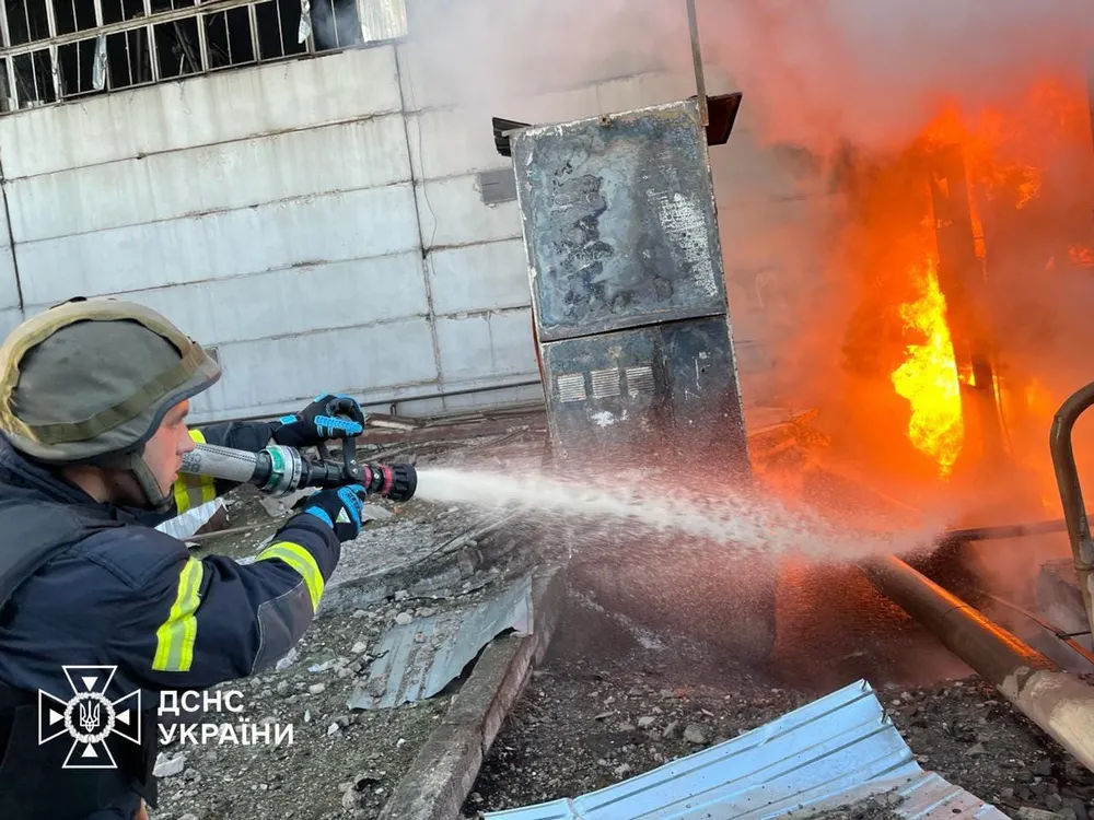 Feuerwehrmann löscht einen Brand am Wärmekraftwerk Trypilska in der Ukraine. Vor ihm schlagen hohe Flammen aus einer beschädigten Anlage.