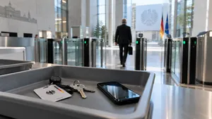 Die Eingangshalle eines Regierungsgebäudes. Im Vordergrund liegen in einer grauen Kunststoffschale ein Dienstausweis mit Bundesadler, ein Schlüsselbund und ein Mobiltelefon. Dahinter geht ein