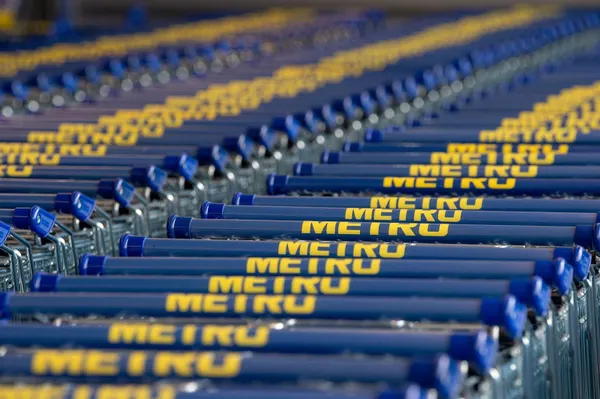 Lange Reihen blauer Einkaufswagen mit gelbem Metro-Schriftzug, dicht ineinandergeschoben, nach hinten in der Unschärfe verschwindend.