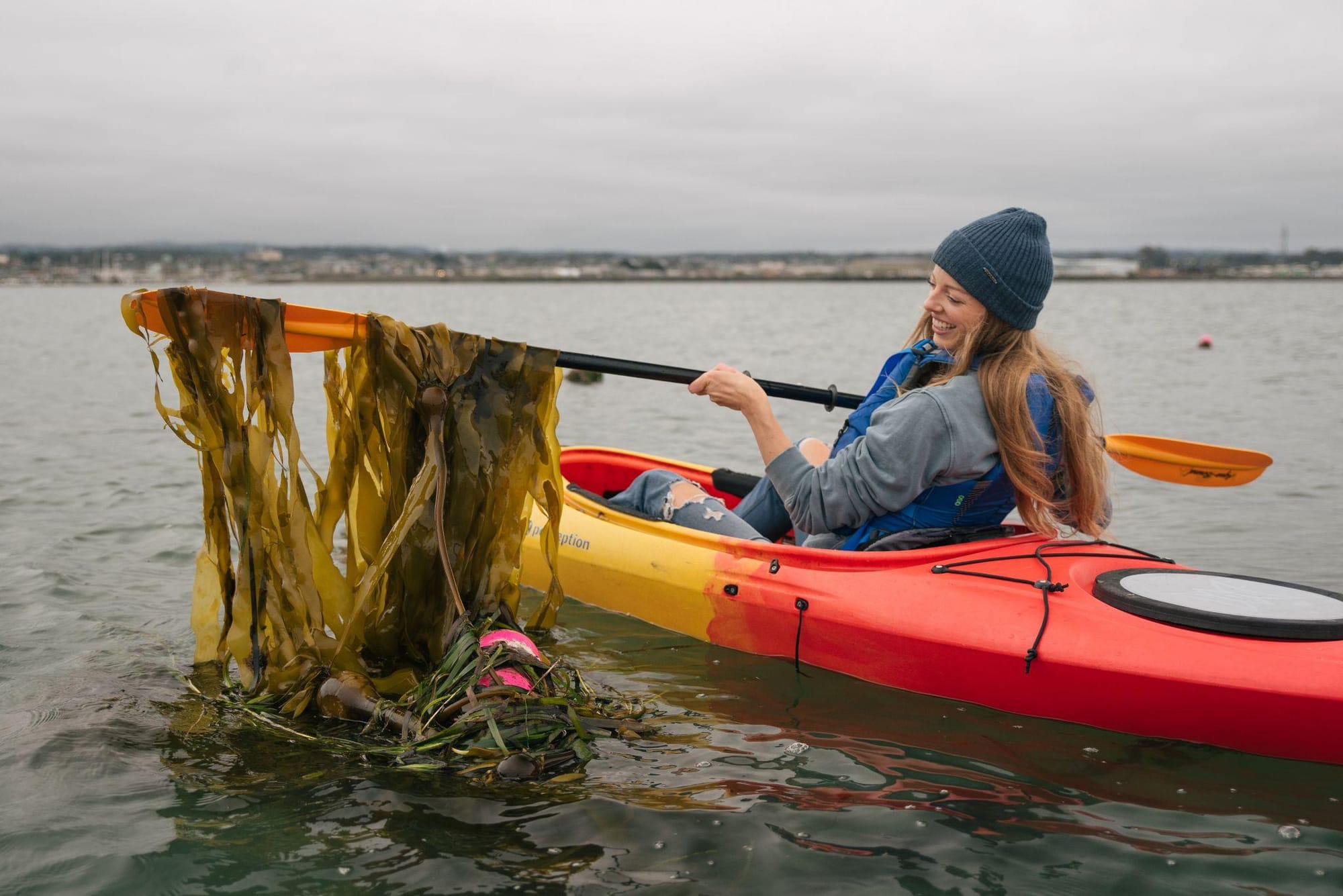 Woman in kayak scooping up seaweed with oar