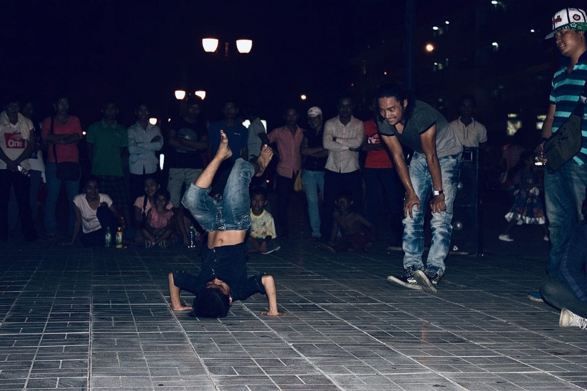 Child performing a breakdance headstand during a lively outdoor street performance, surrounded by a crowd