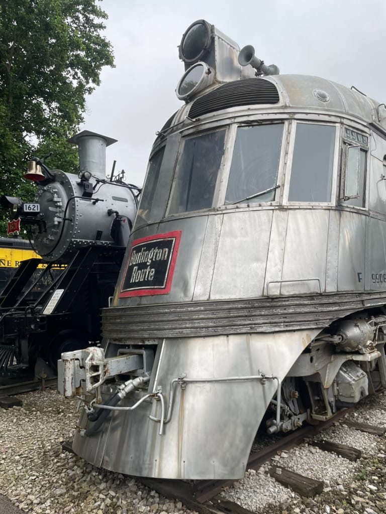 A silver streamlined locomotive. The front says "Burlington Route" in a white font on a black background with a red border
