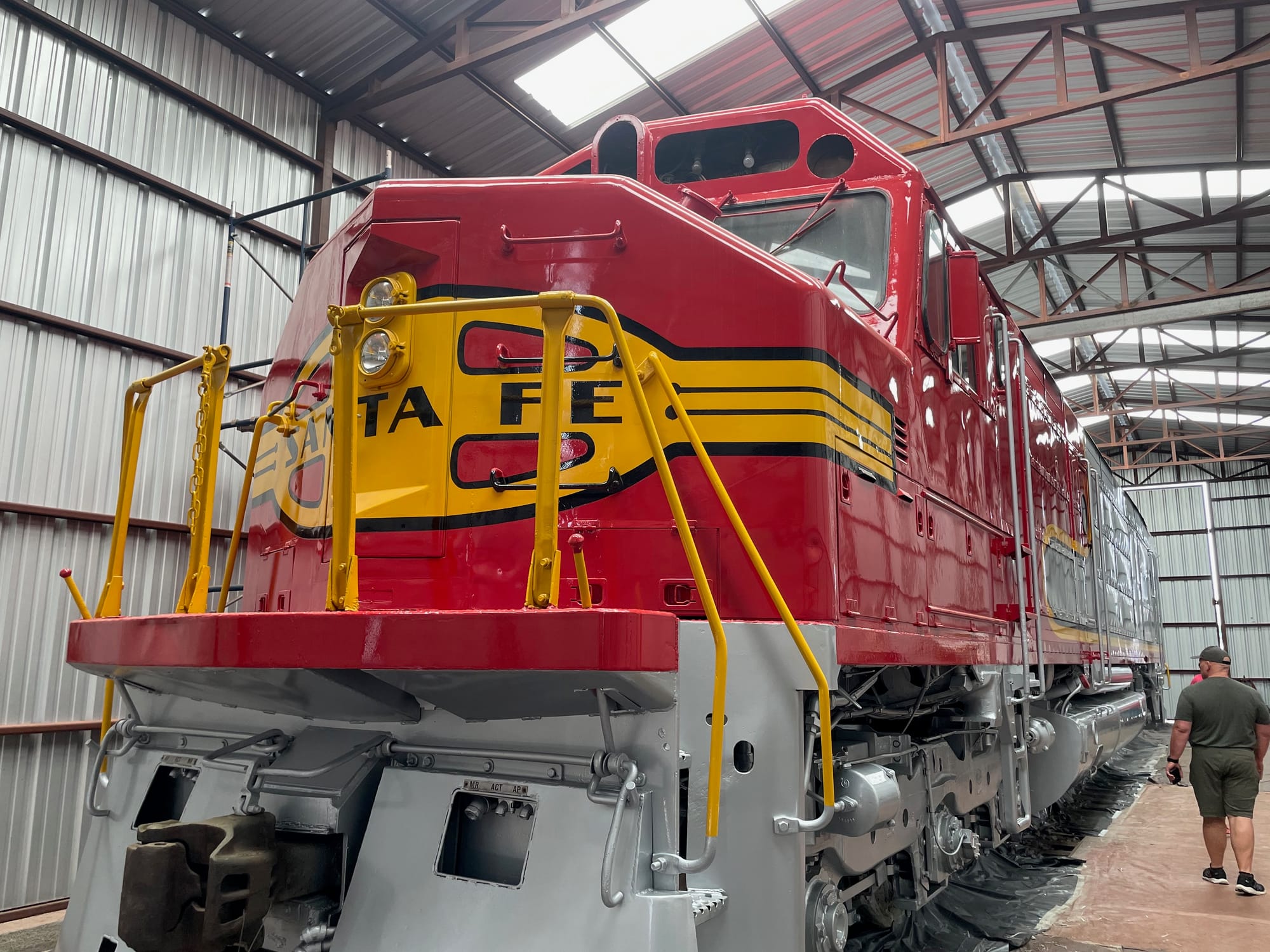 An FP45 Diesel electric locomotive. We're looking at the front and part of the side. The nose is red like a bonnet with a yellow patch that says "Santa Fe". There are yellow handrails. The front plow and wheels are painted silver. The locomotive is missing its top headlights and number boards