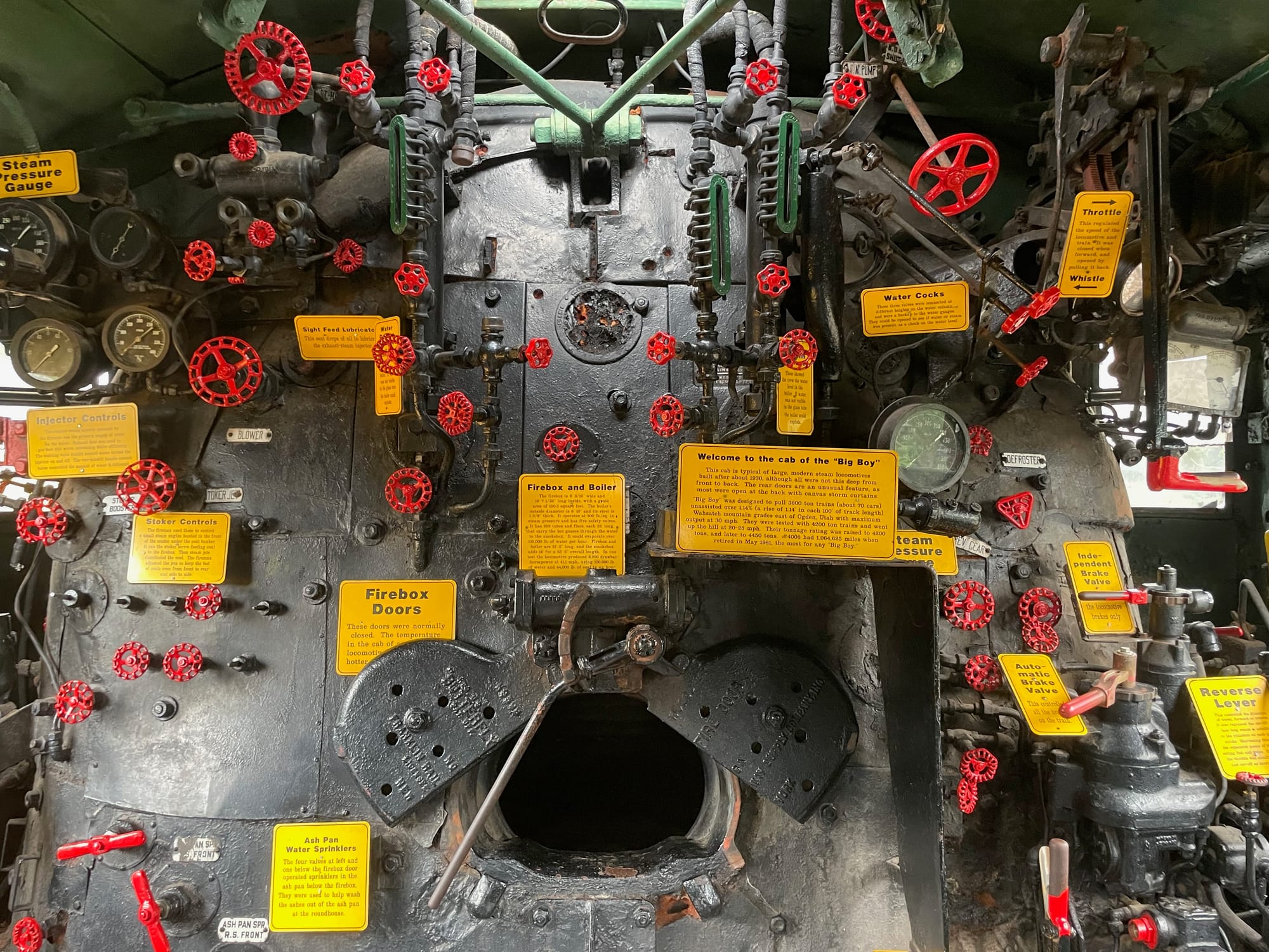 A steam locomotive cab interior. All of the controls are labeled with yellow signs describing them (there are a ton)