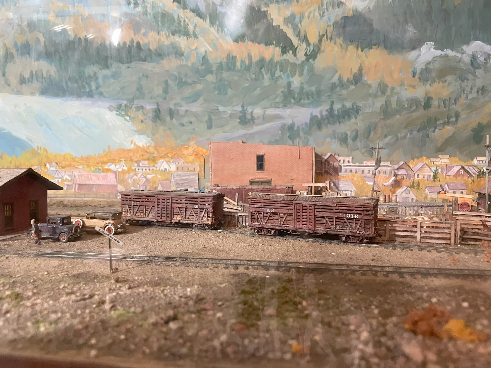 A railroad scene where two cattle cars are waiting to be loaded in front of a town and a painted mountain backdrop