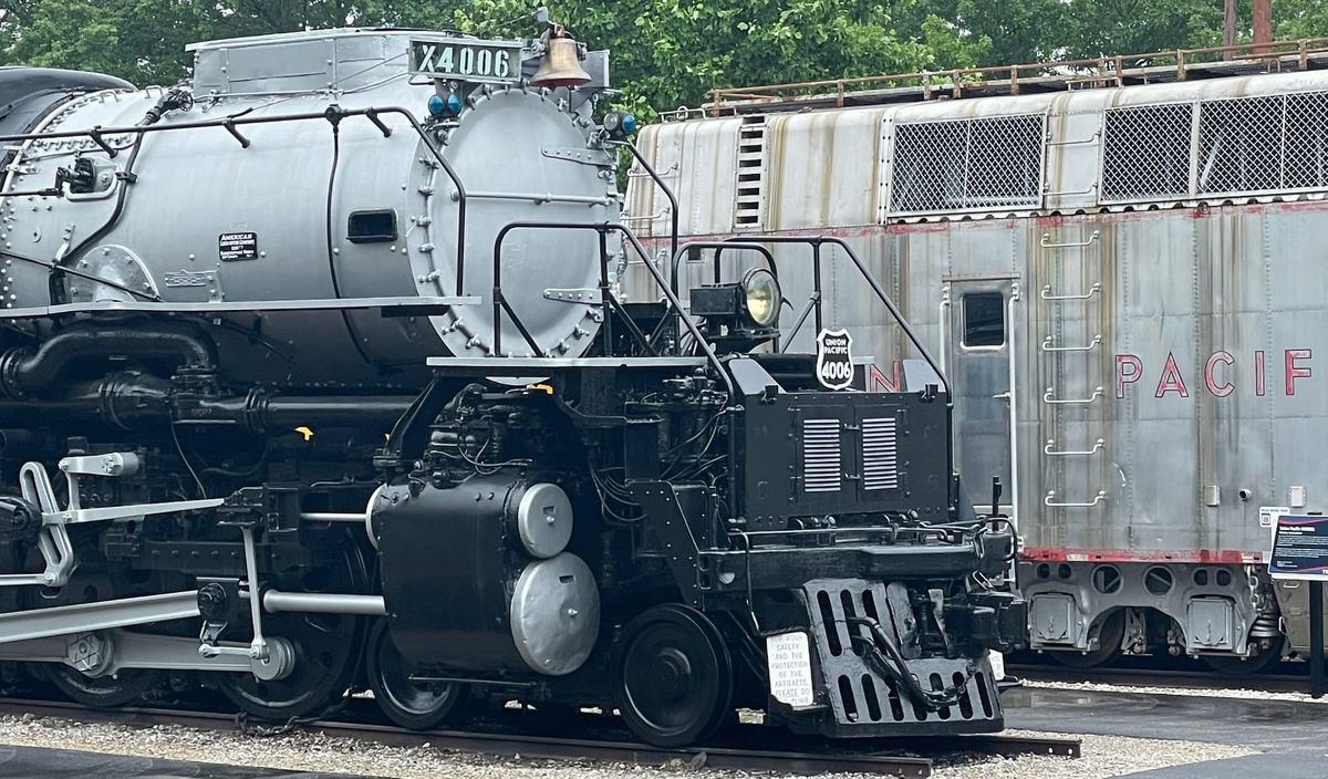 The front-right of a large steam locomotive. It has a silver boiler and black frame