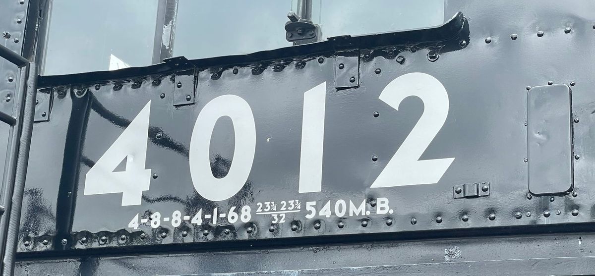 The cab of a black steam locomotive. The number in white is 4012 under a glass window. The rivets are visible in two rows running left and right, above and below the numbers.
