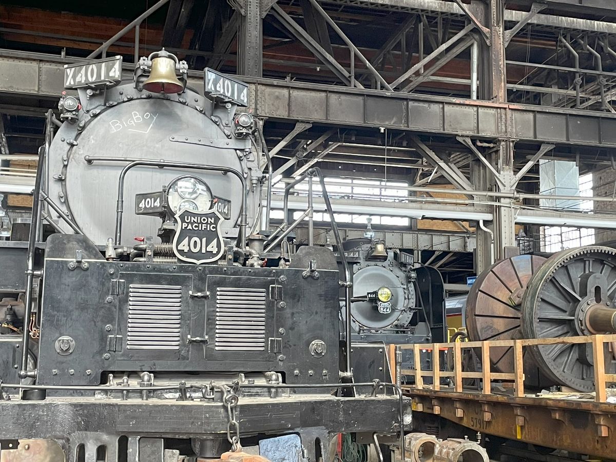 A pair of steam locomotives. Foreground 4014 in gray and sliver. Background 844 in gray and sliver. There's a flatcar with equipment in front of 844. 