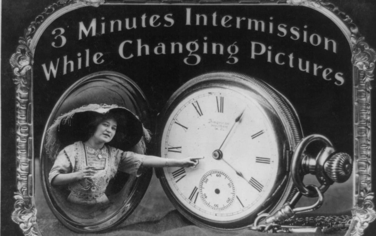 Photo shows woman pointing at pocket watch dial used for intermission in an old movie theater. Text reads "3 Minutes Intermission while changing pictures"