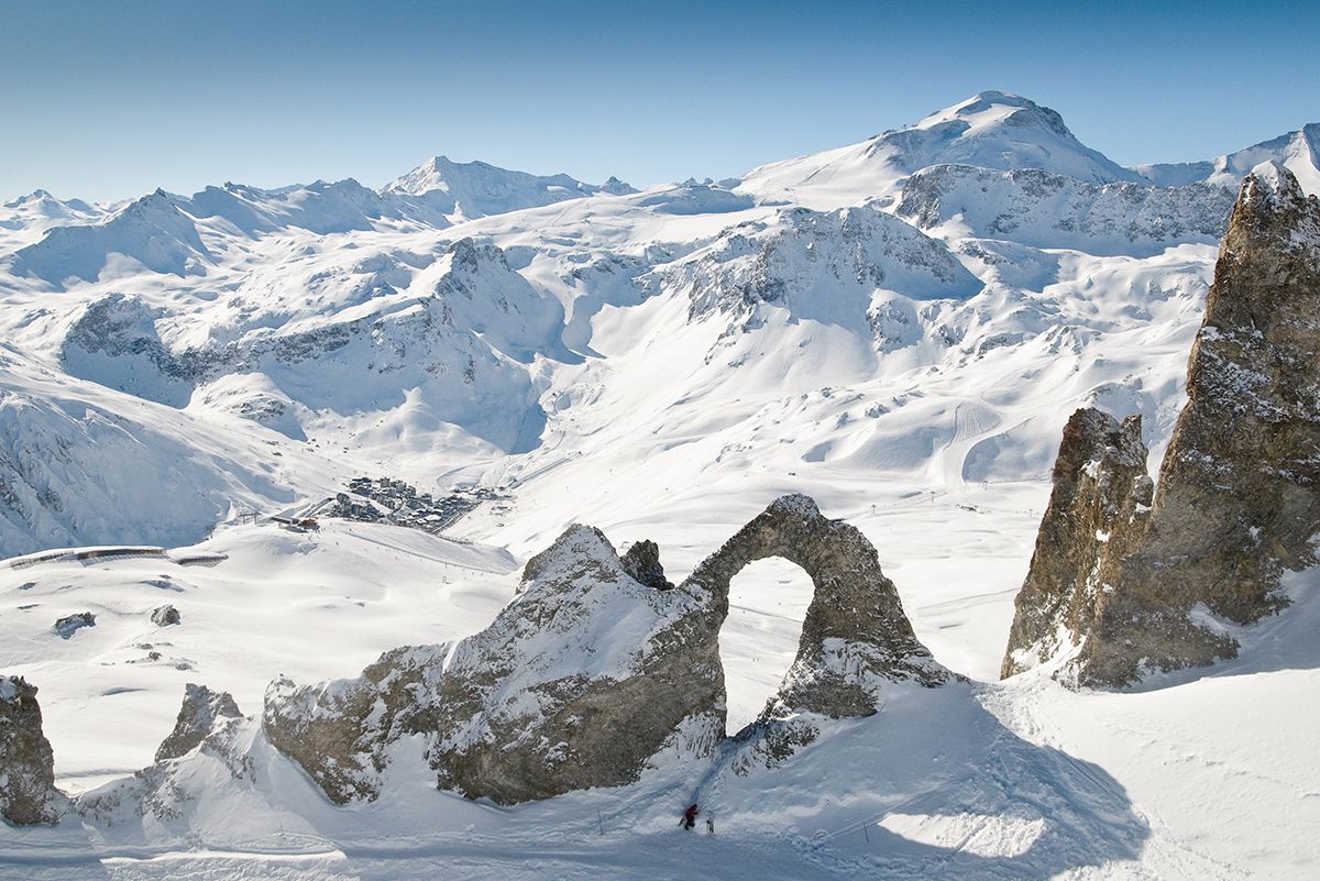 a rock with a giant hole through it with feet tracks walking in the snow through the hole in Val d’Isere-Tignes