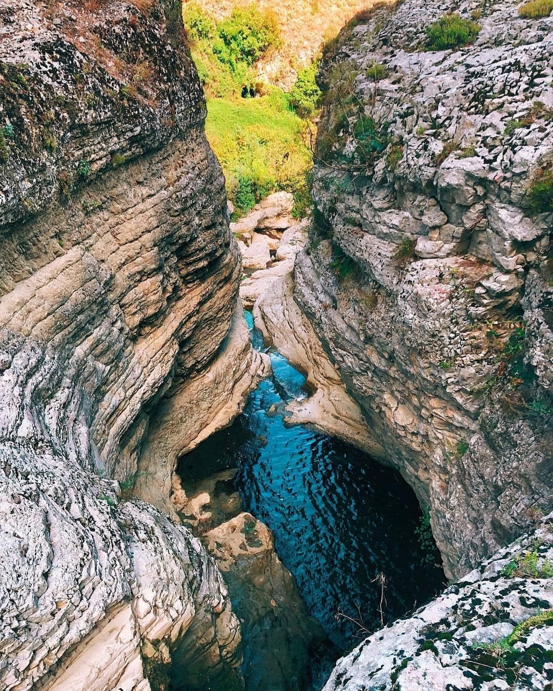 Blue water flowing through Gjipe Canyon in southern Albania, surrounded by steep rock walls and lush greenery near the Ionian coast.