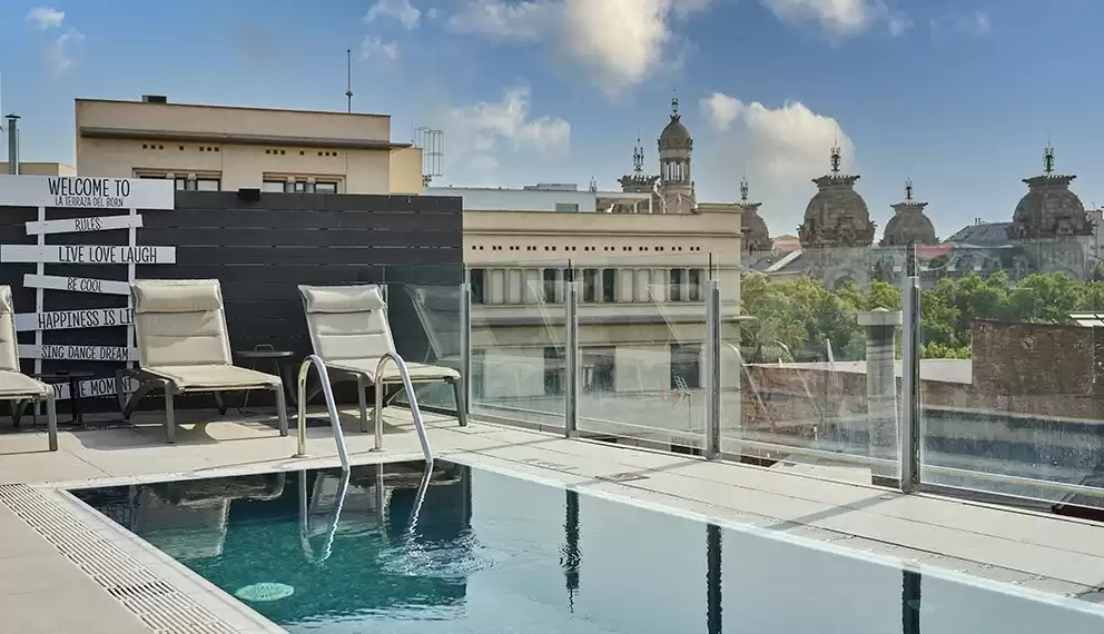 Rooftop pool at Catalonia Born Hotel in Barcelona with lounge chairs and panoramic views of the city’s historic architecture.