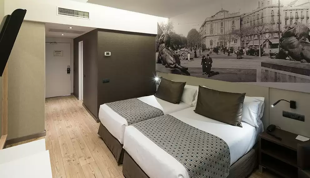 Modern hotel room at Catalonia Born in Barcelona featuring twin beds, neutral tones, and a mural of a historic city street.