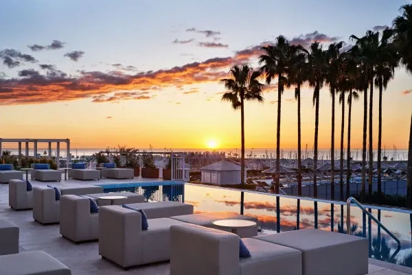 Sunset view from the rooftop terrace at Hotel Arts Barcelona featuring palm trees, a reflection pool, and Mediterranean Sea views.