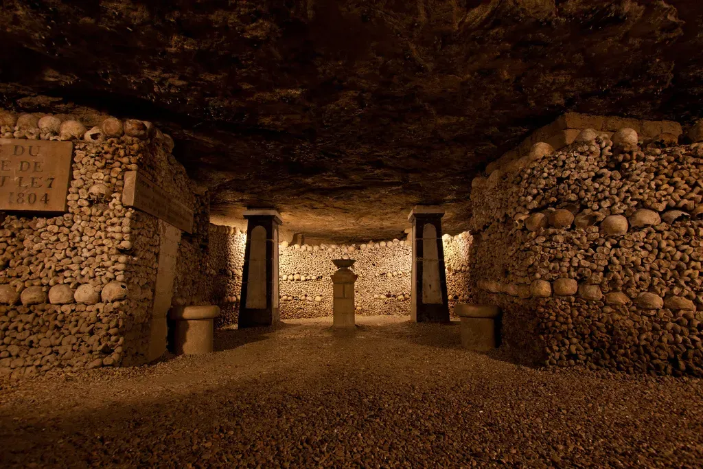 inside the Paris Catacombs with bones and skulls making the walls, and there is an entrance to another part of the catacombs. 