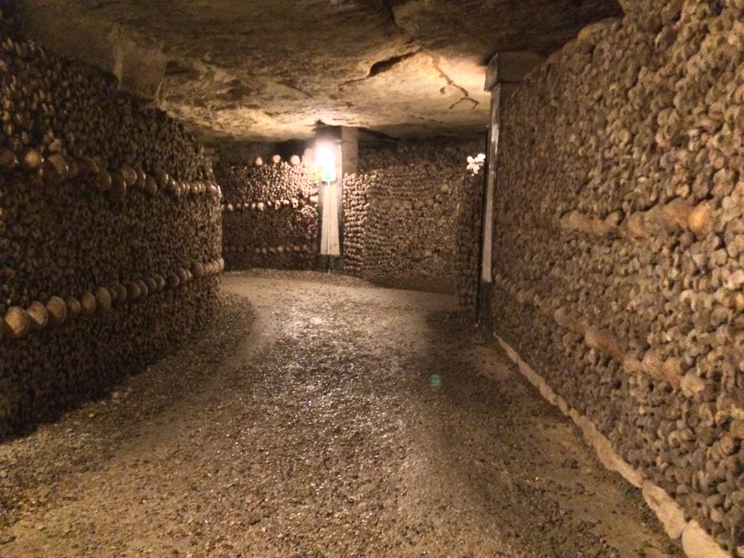 Inside tunnel of the Paris Catacombs with bones and skulls lining the walls. 