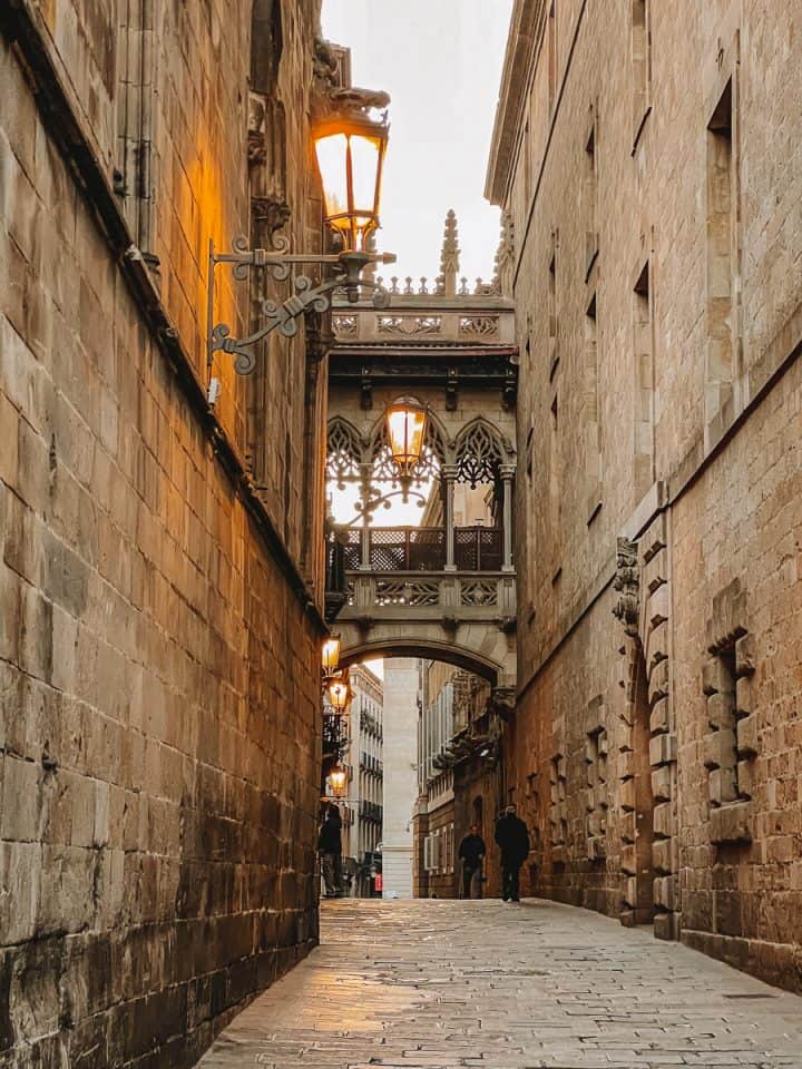 Cobblestone streets with two people walking between buildings that Bishop Street Bridge connects the buildings above them.