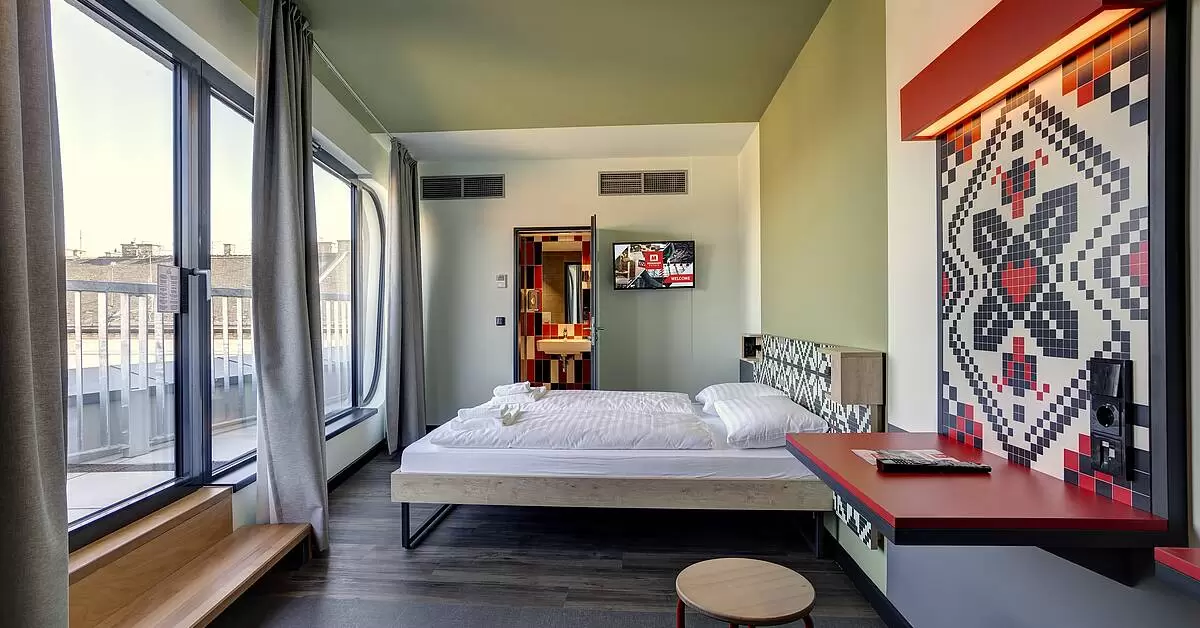 Hotel room with glass doors leading out to a balcony with a queen bed and art work on the wall.