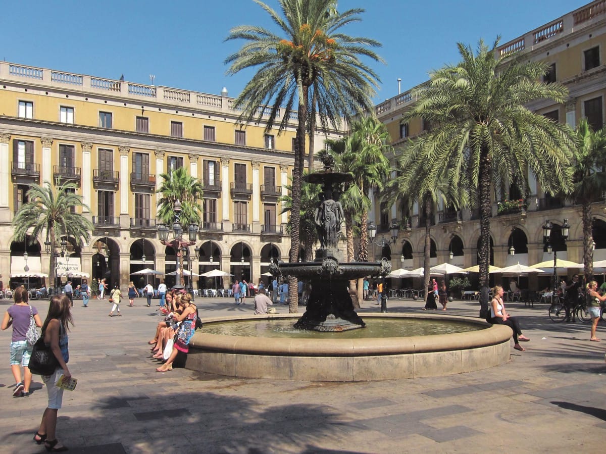 People sitting around a fountain in Royal Square Plaça Reial in Barcelona's Gothic Quarter.