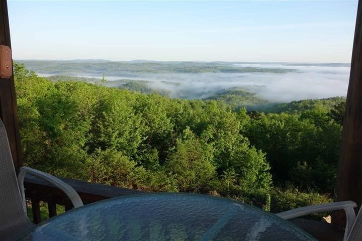 Looking out over a vast distance from on top of a mountain and the land below is covered in a mist from the early morning mist cause by Current River down below. 