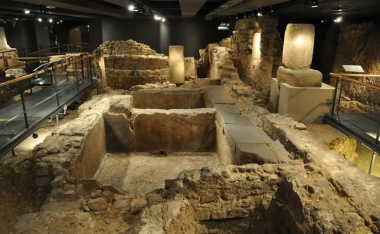 Excavated ruins of the Roman Temple of Augustus in Barcelona, with stone columns and walls in a museum, walkways above.