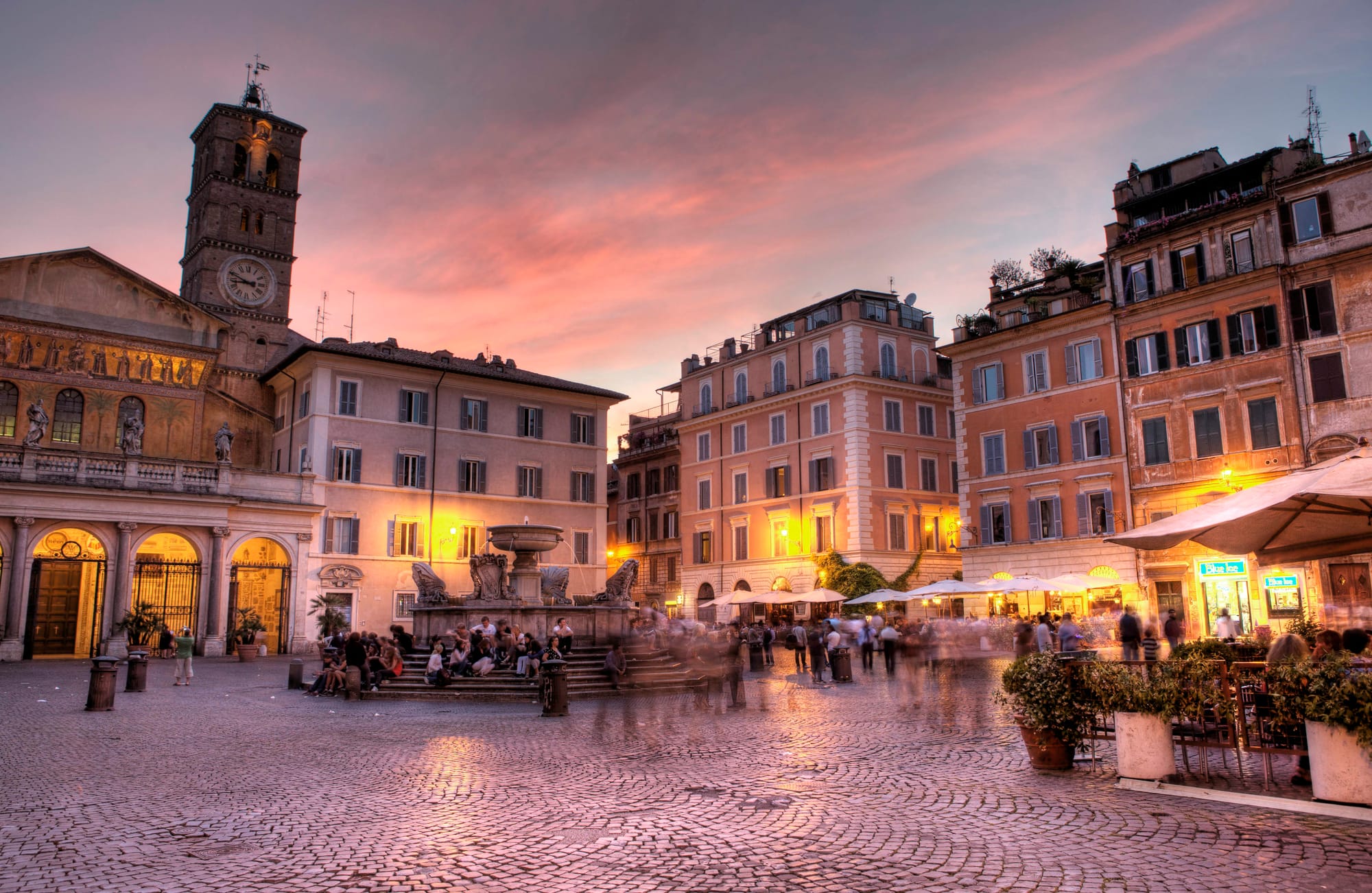 People walking around on cobblestone streets in a town square in the Trastevere neighborhood of Rome.