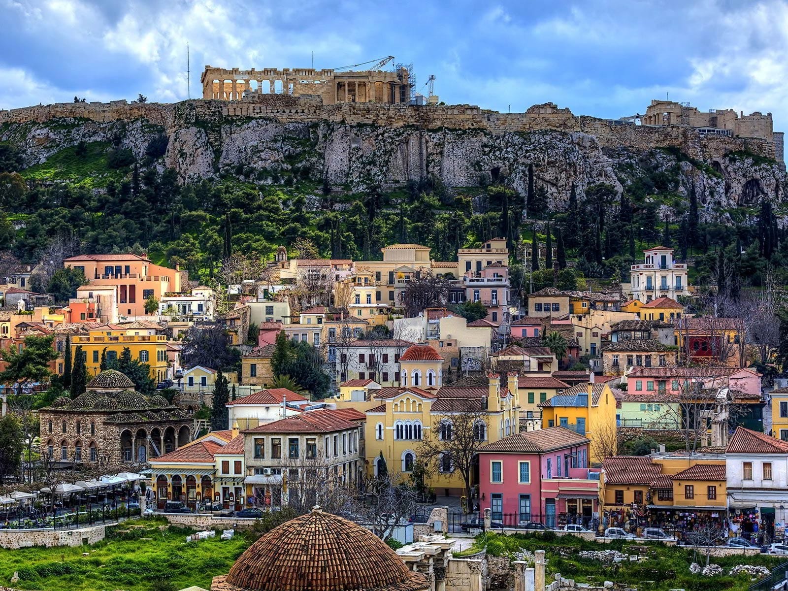 A Greek neighborhood with colorful houses in Athens known as Plaka sits next to an old fortified cliff in the city.
