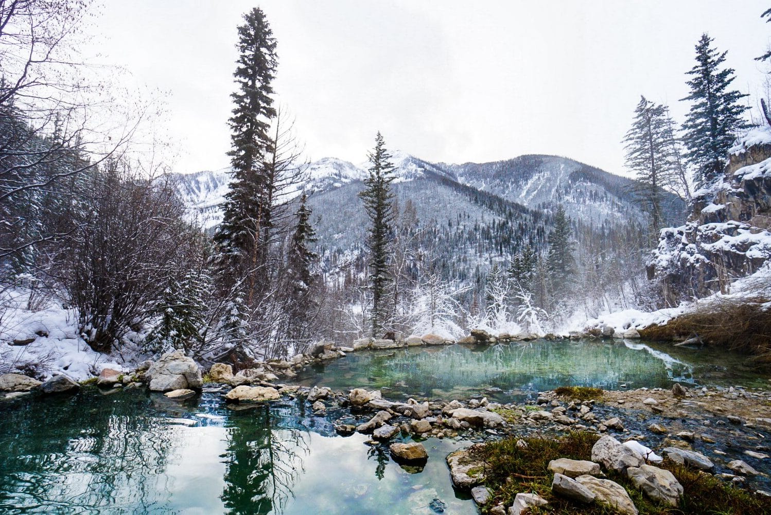 Steam coming of of two pools of hot springs surrounded by snow inside Banff National Park.