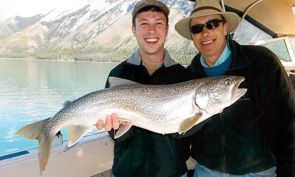 A man posing next to his father and holding a large trout he just caught.