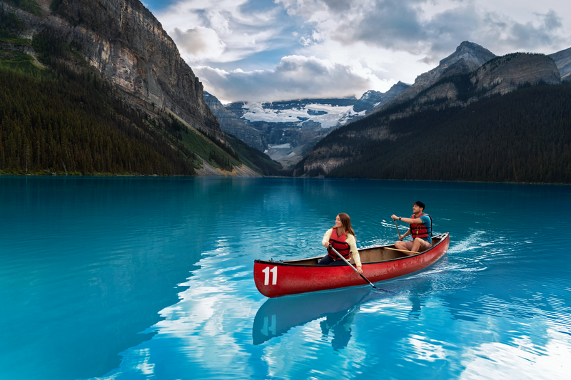 Two people in a red canoe crossing a beautiful lake that is surrounded by mountains. 