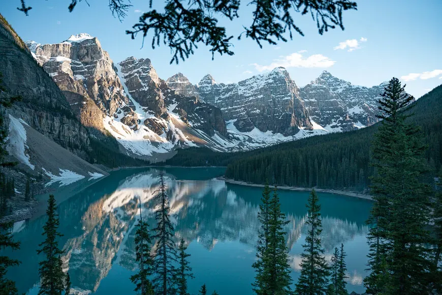A view looking down at Moraine Lake inside Banff National Park shows a pretty lake surrounded by large snow covered mountain peaks.