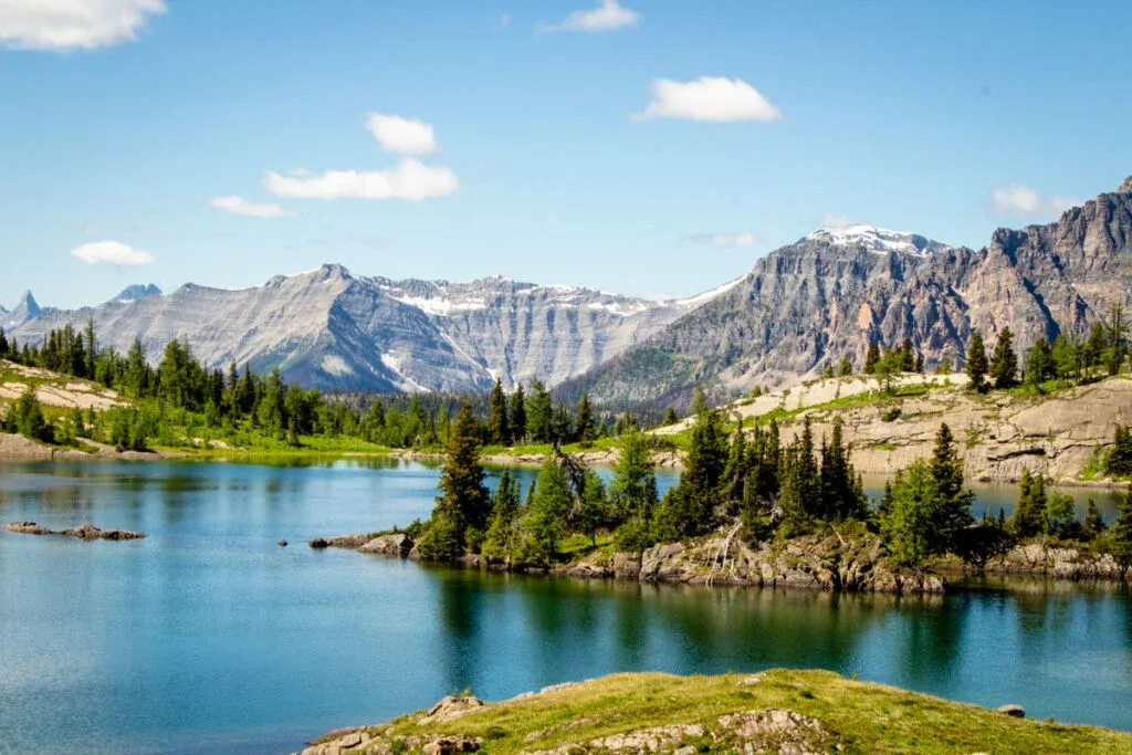 A lake with an rock island covered in trees in the center, with views of large mountains surrounding the lake.