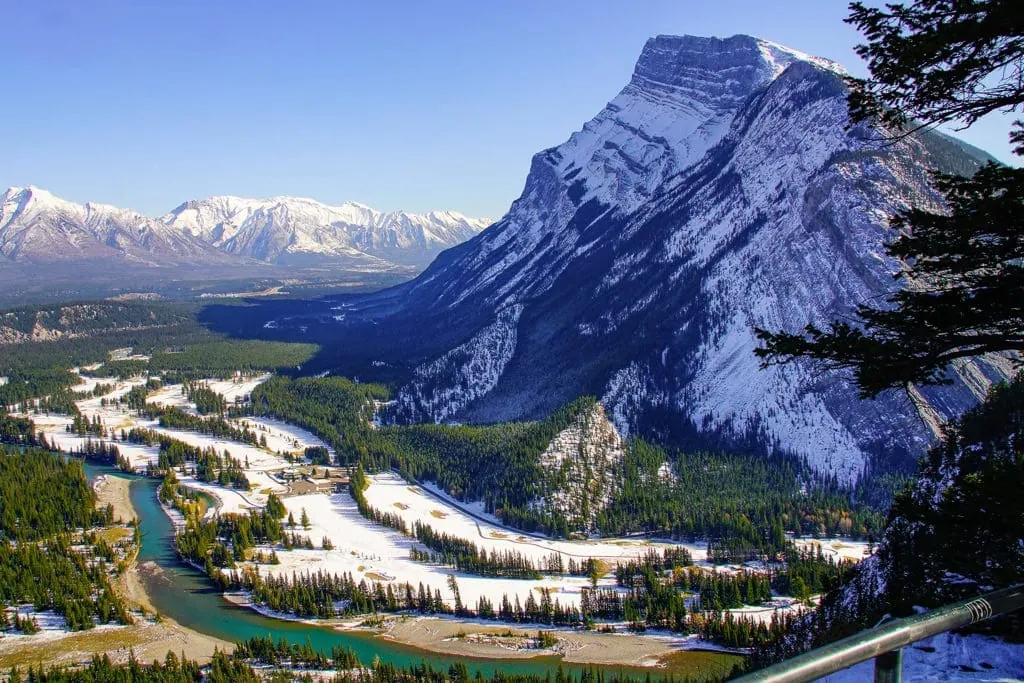 A river running through partially snow covered valley beside a large mountain inside Banff.