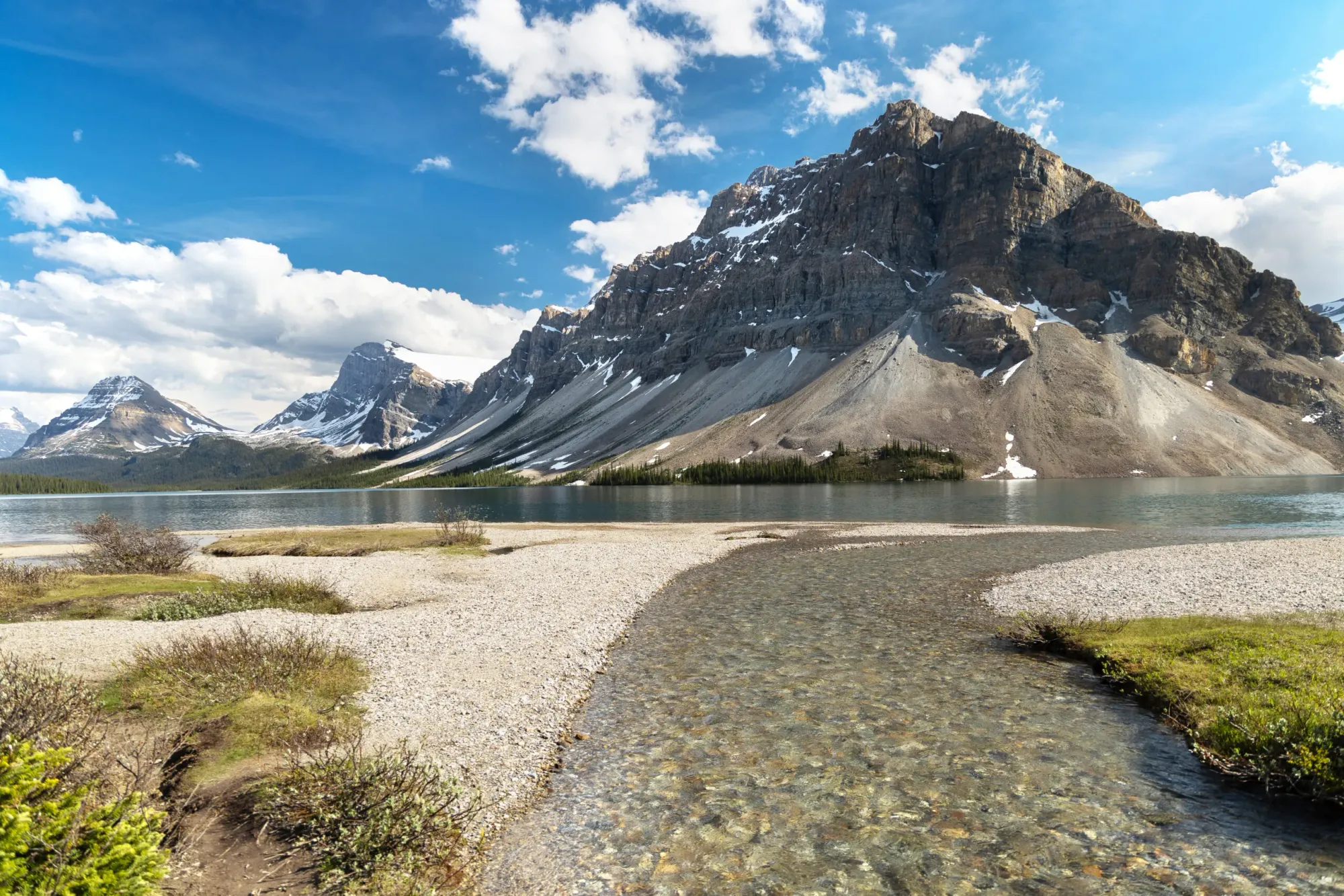 A clear stream of water is running into a lake that is surrounded by beautiful mountains. 