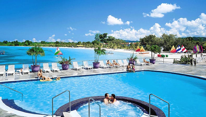 Two people in a hot tub, and other guide in the swimming pool with ocean views at Grand Lido Negril Au Naturel Resort, in Negril, Jamaica.