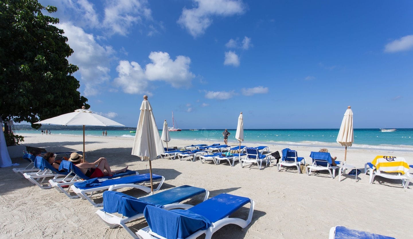 Beautiful beach with blue chairs and white umbrellas at Tree House Resort on Negril's 7-mile beach.