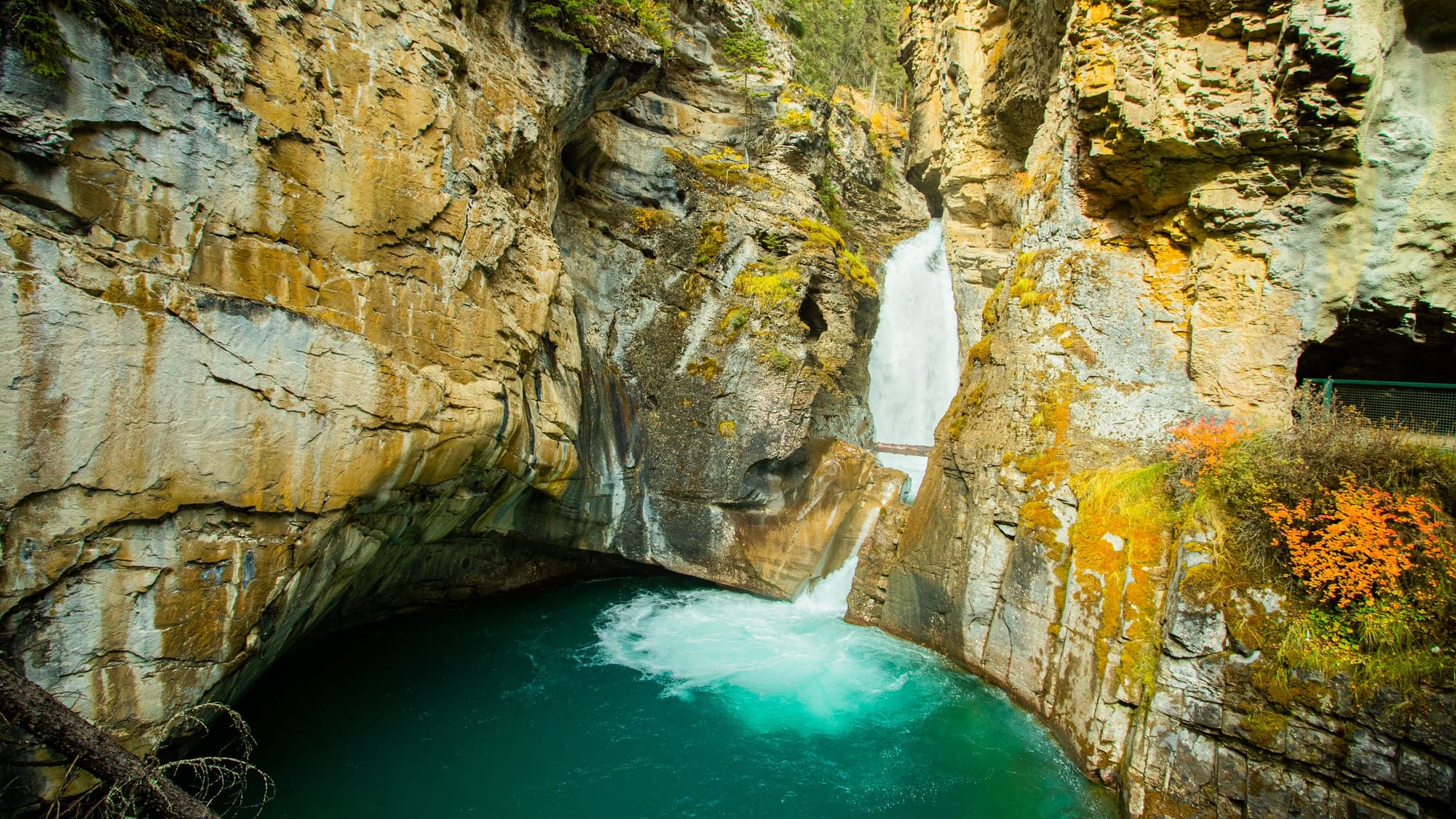 A small water fall running down a rocky mountain and into a round pool of turquois waters.
