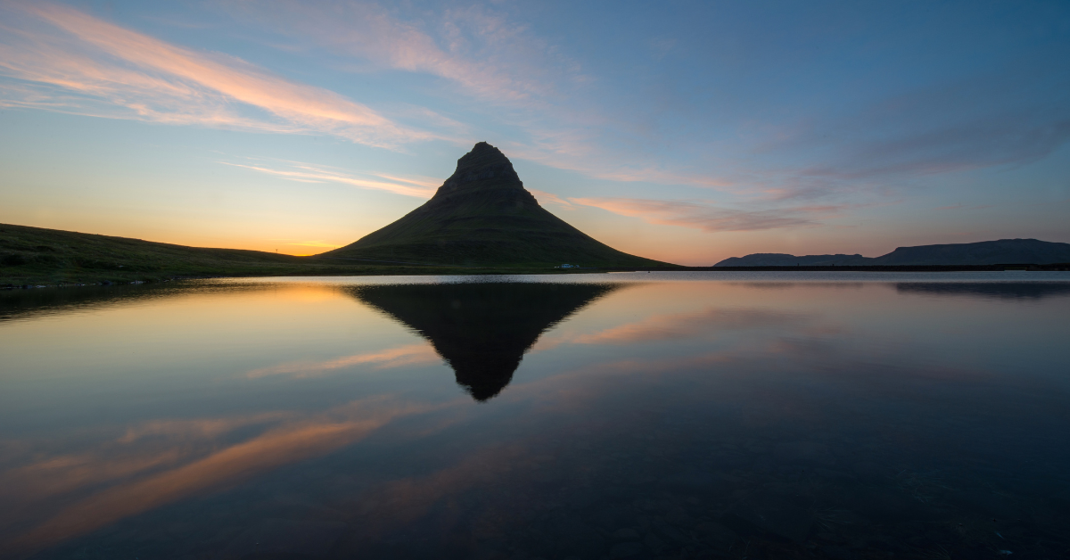 Waters so calm it looks like glass with a Kirkjufell mountain reflecting off of the waters at sunset.