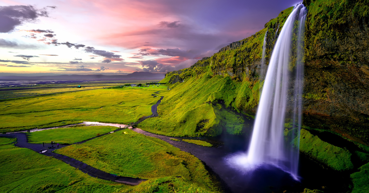 Seljalandsfoss waterfall is a large waterfall that lands into a pool of water and turns into a river that runs through lush bright green plains in Iceland.