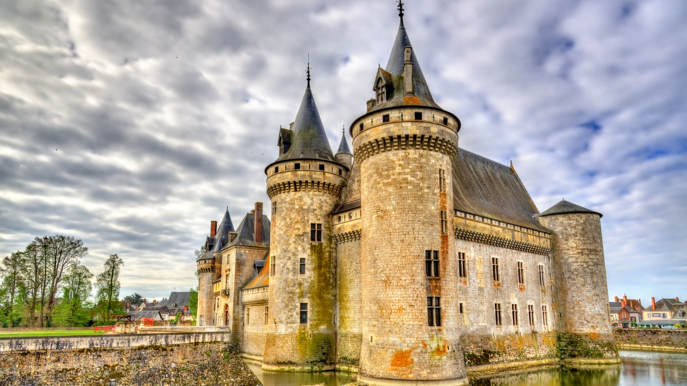 Medieval stone château with round towers and a moat in the Loire Valley, France, under a dramatic cloudy sky with reflections in the water.