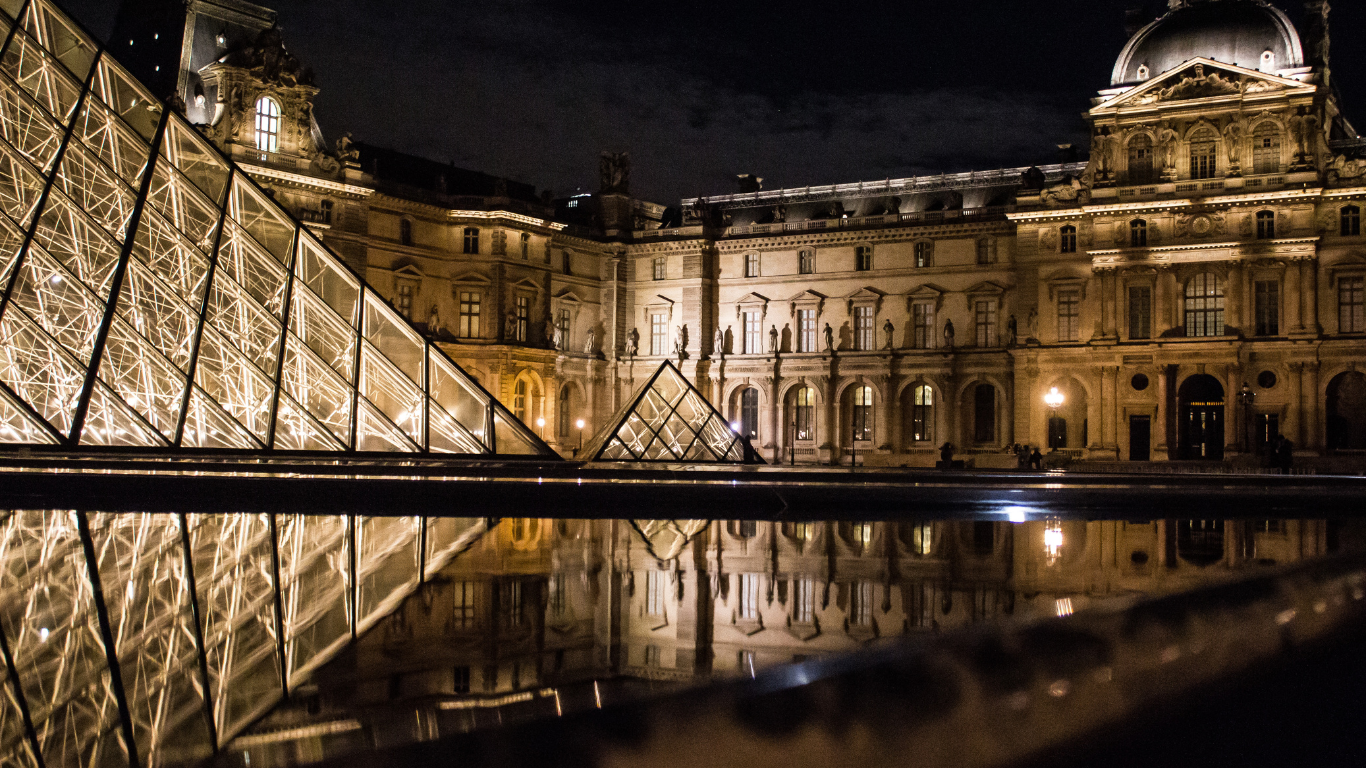 The Louvre Museum at night with lights reflecting off the wet concrete.