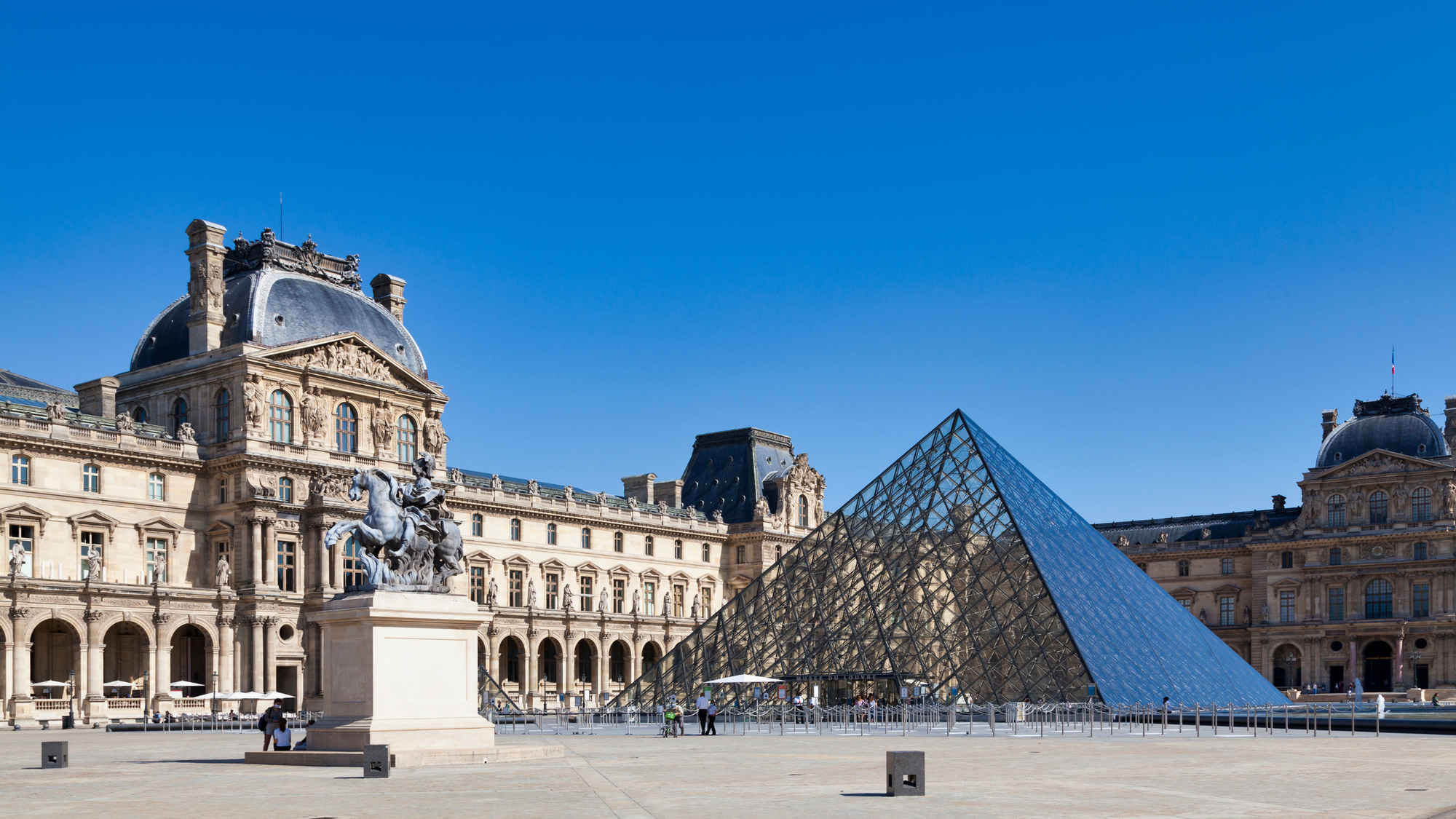 The Louvre museum in Paris, France with a glass pyramid under a blue sky.