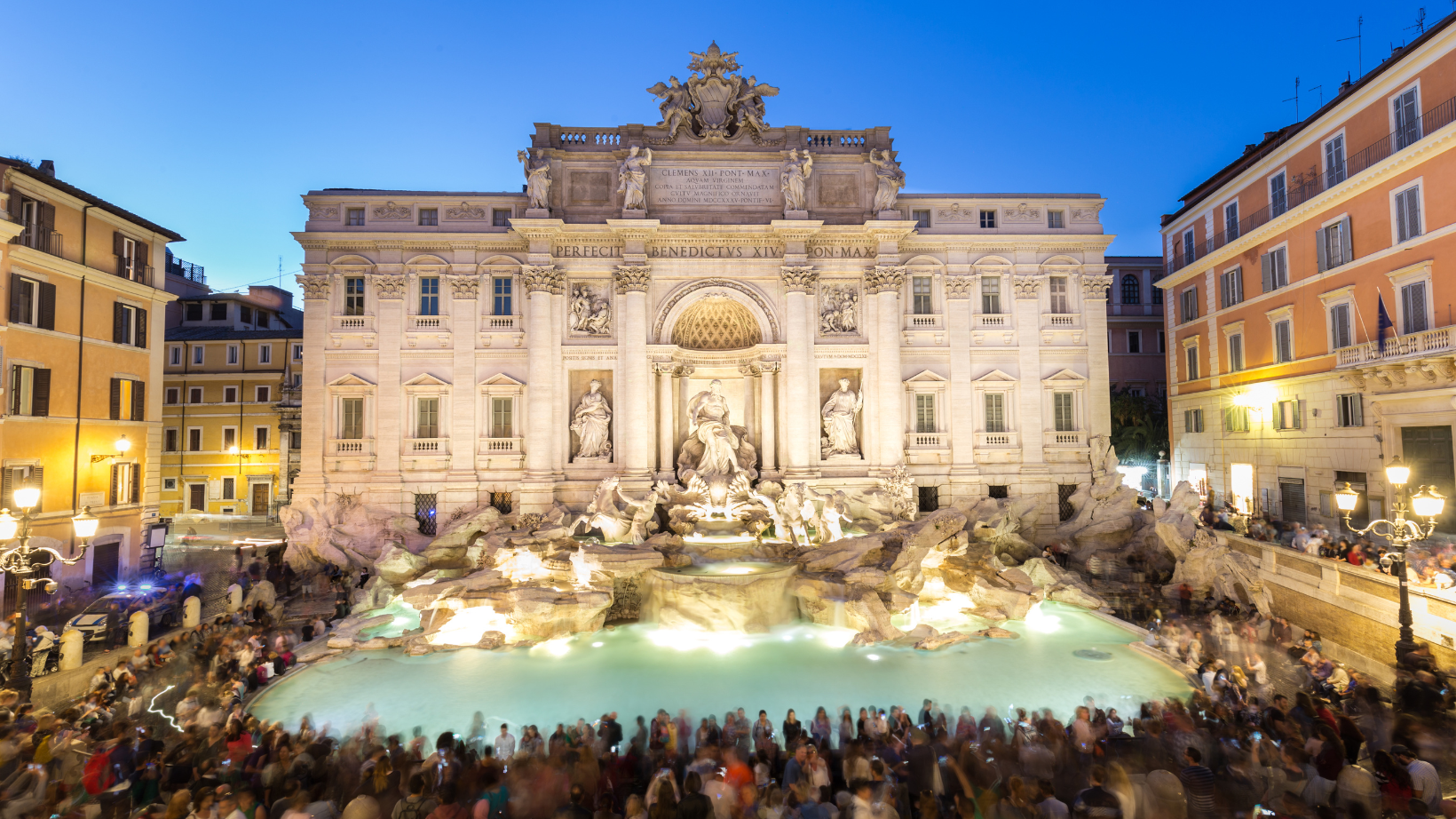 People surrounding Trevi fountain in Rome at night.