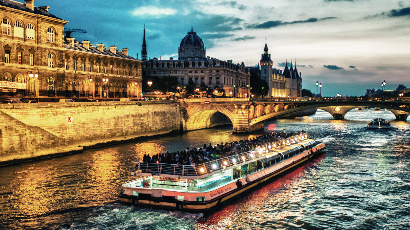 Dinner cruise on the Seine River crossing under a bridge with the city of Paris in the background at sunset.