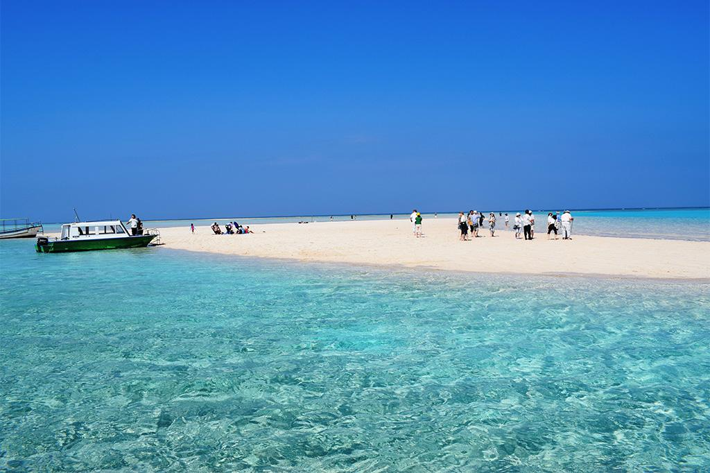 A boat parked on a white sand beach that has formed an Island, with people enjoying a day at the beach.