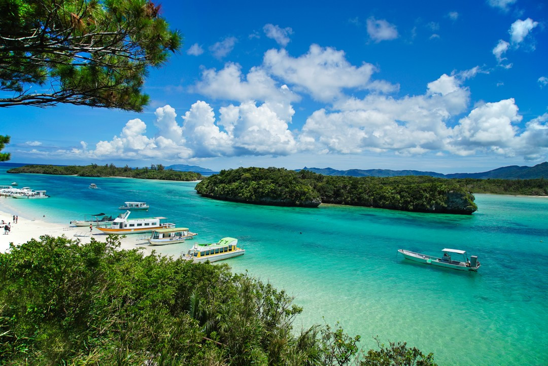 A boat is taking people for a ride in beautiful waters, and more boats are parked on the beach.