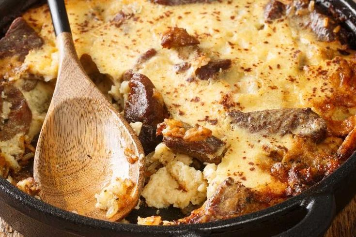 Tavë Kosi dish in a pan with cheese and beef with a spoon laying on top of it